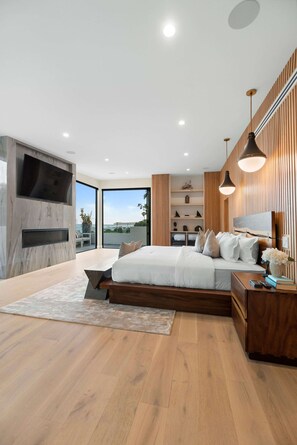 A modern bedroom with a large bed, built-in TV, and a view of the outdoors. - Sea Vista (Malibu)