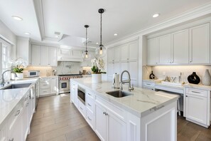 A spacious kitchen with white cabinetry, a large island with a sink, and modern appliances. - Emerson Estate (Sherman Oaks)