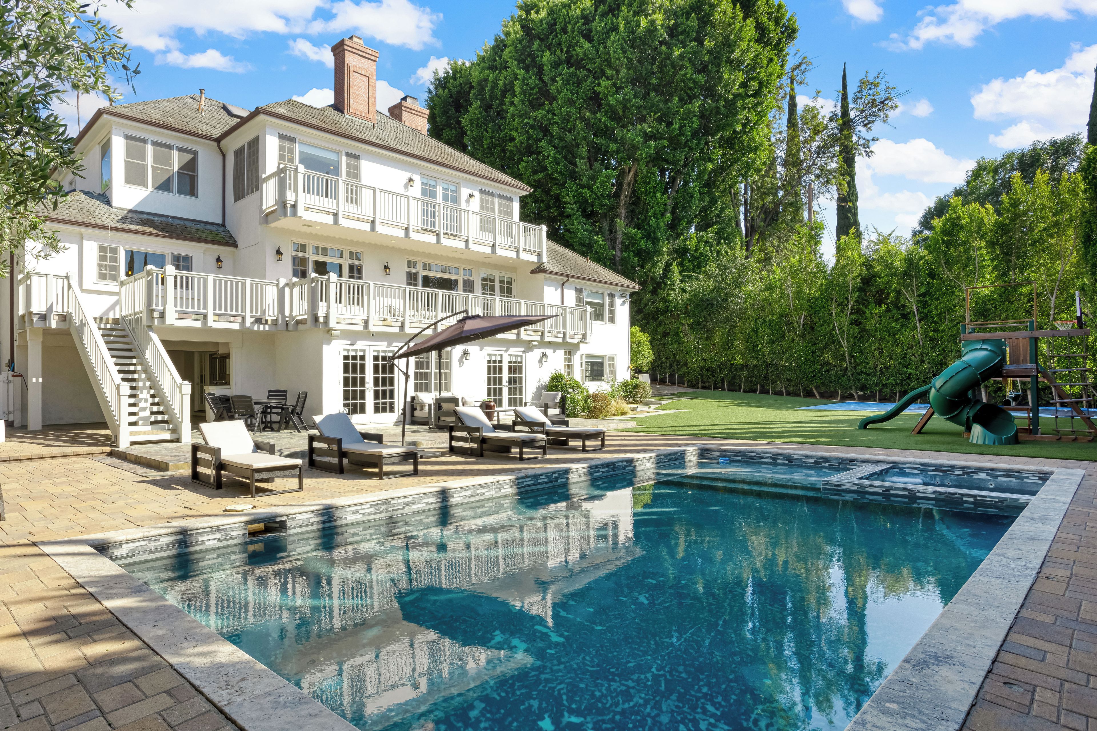 A two-story house with a swimming pool, outdoor furniture, and a slide.