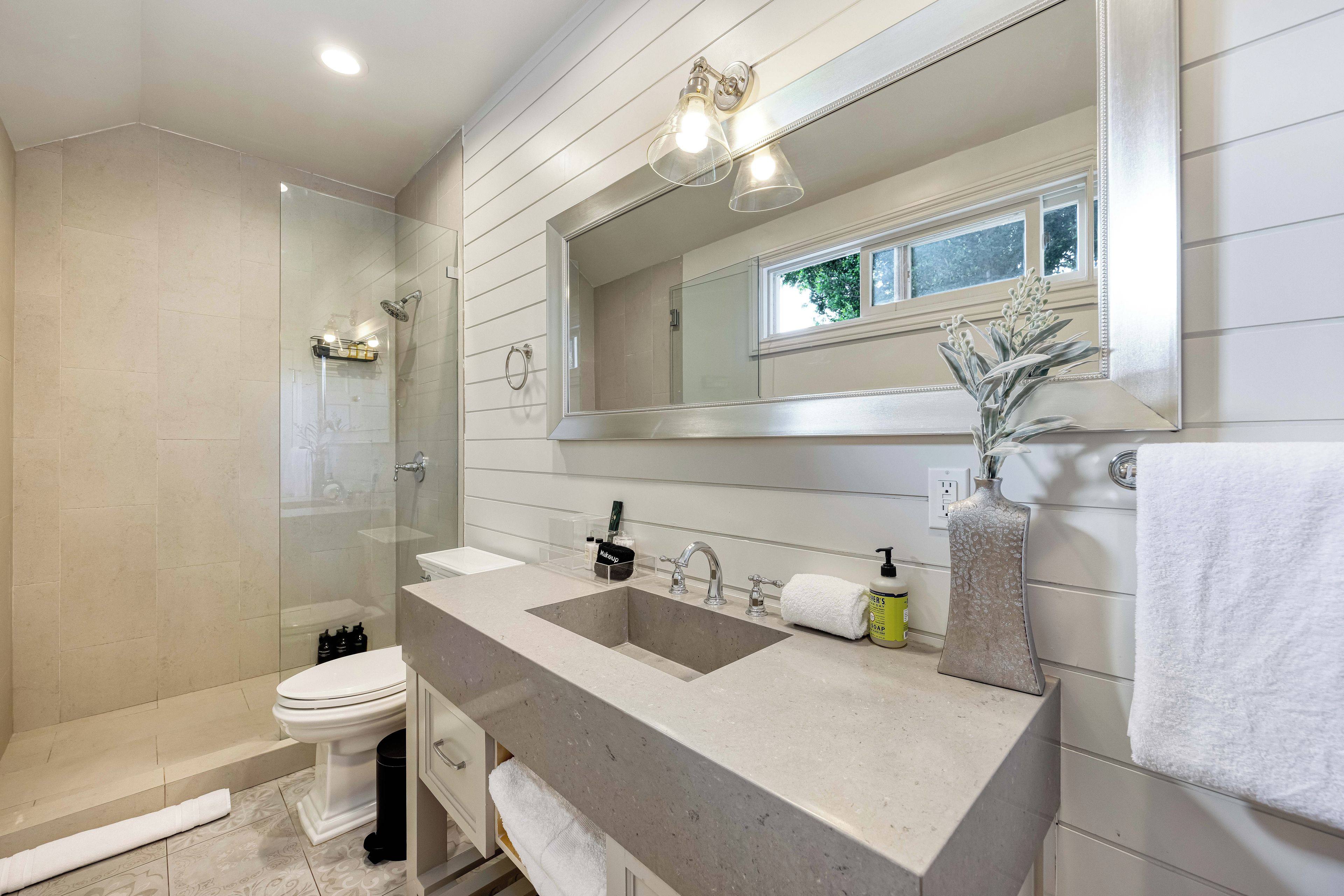 A modern bathroom with a glass-enclosed shower, a vanity with dual sinks, a toilet, and a large mirror.