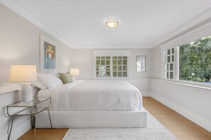 Un dormitorio amplio con una cama grande, dos lámparas de noche, un cuadro enmarcado en la pared y una ventana con vistas a zonas verdes.