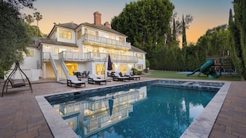 A two-story house with a swimming pool, outdoor seating, and a slide.