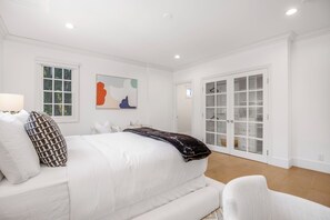A bedroom with a large bed, white walls, a window, and a sliding glass door leading to a closet. - Emerson Estate (Sherman Oaks)
