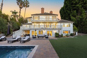 Una casa de dos pisos con piscina, mobiliario exterior y un césped bien cuidado.
