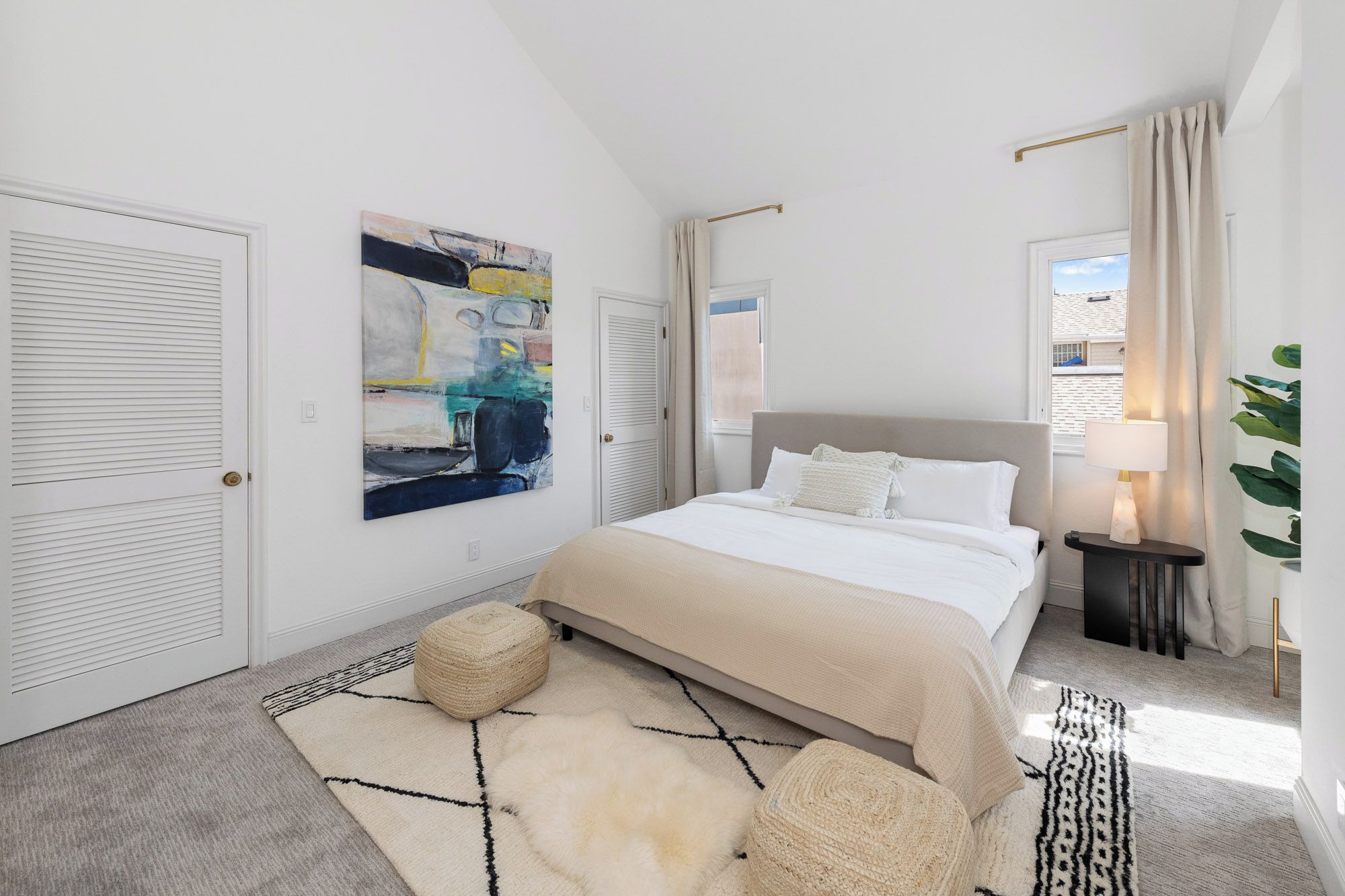 Een slaapkamer met een bed, een schilderij, een raam en een plant.