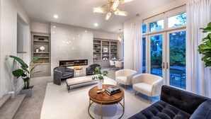 Una sala moderna con chimenea, una mesa de centro, sofás y un comedor visible a través de amplios ventanales.
