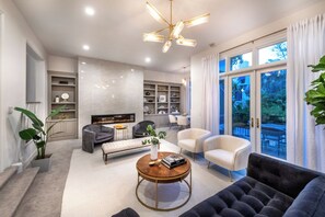 Una sala moderna con chimenea, una mesa de centro, sofás y un comedor visible a través de amplios ventanales.