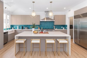 A modern kitchen with a large island, bar stools, stainless steel appliances, and pendant lighting. - Reef Mall (Marina del Rey)