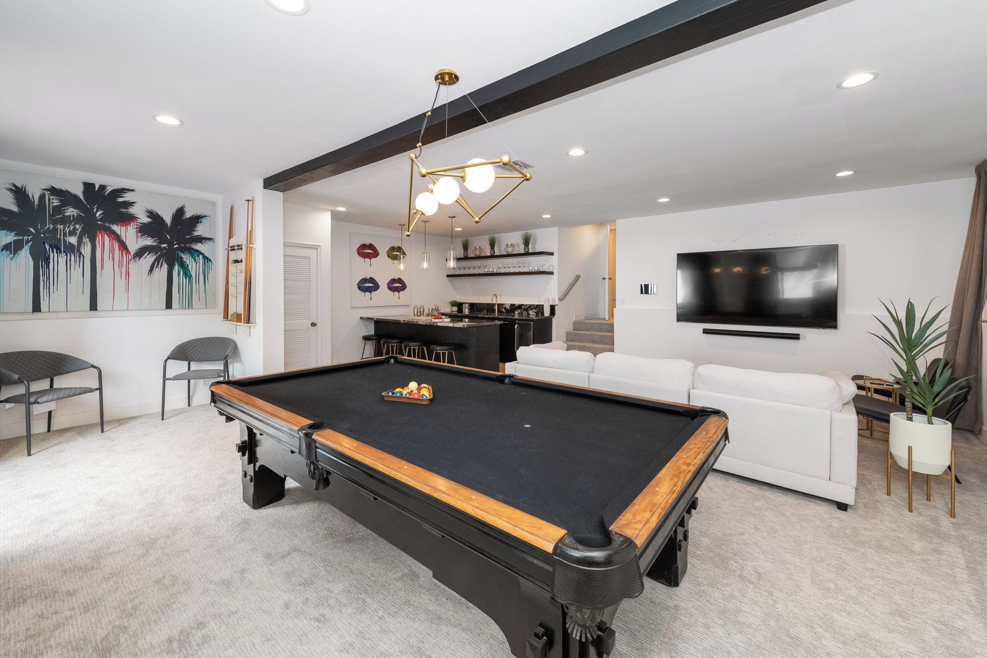 Een moderne woonkamer met een pooltafel, een witte bank, een televisie en een keuken.