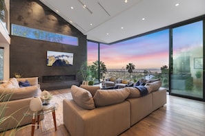 A modern living room with a large sofa, a flat-screen TV, and a city view through large windows. - Franklin Modern (West Hollywood)