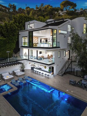 Una casa moderna de varios pisos con piscina, mobiliario exterior y una escalera que lleva a los niveles superiores.
