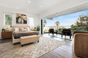 A bedroom with a bed, a bench, a nightstand, a painting, and a view of the outdoors. - Franklin Modern (West Hollywood)