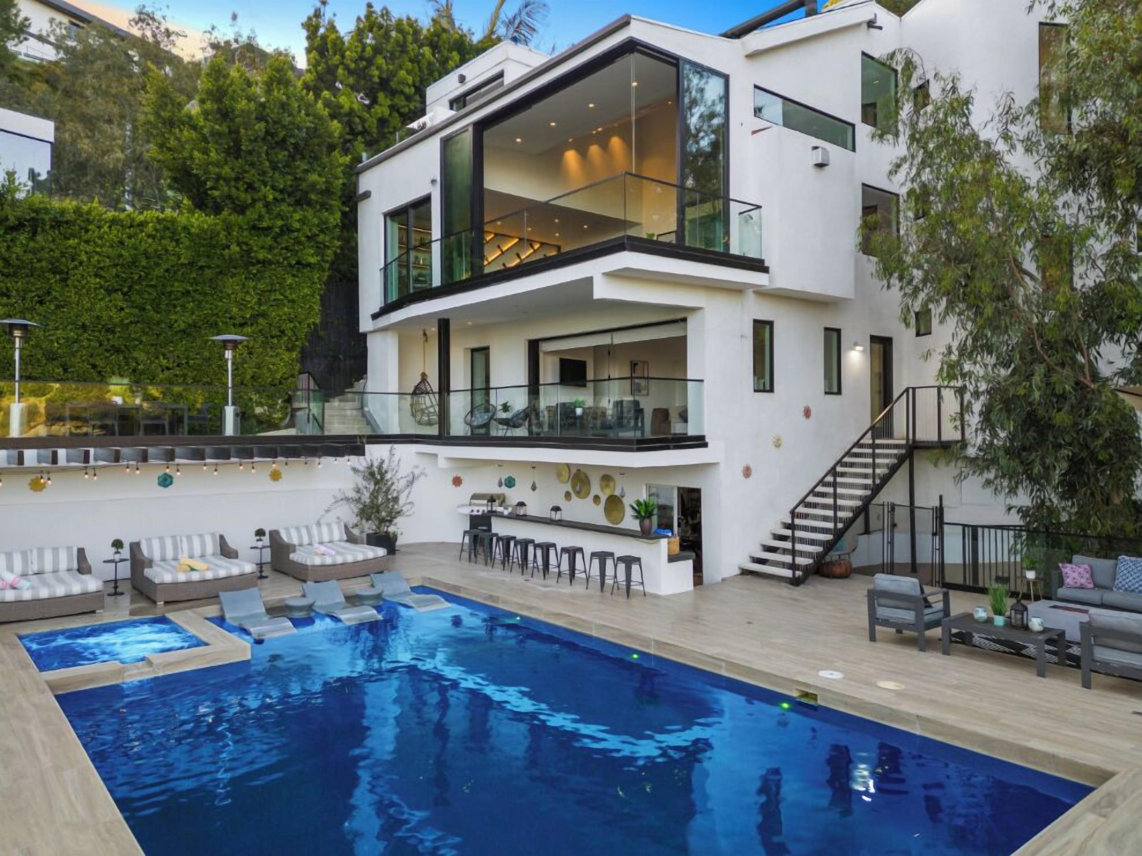 A modern two-story house with a swimming pool, outdoor seating, and a staircase leading to the upper level.