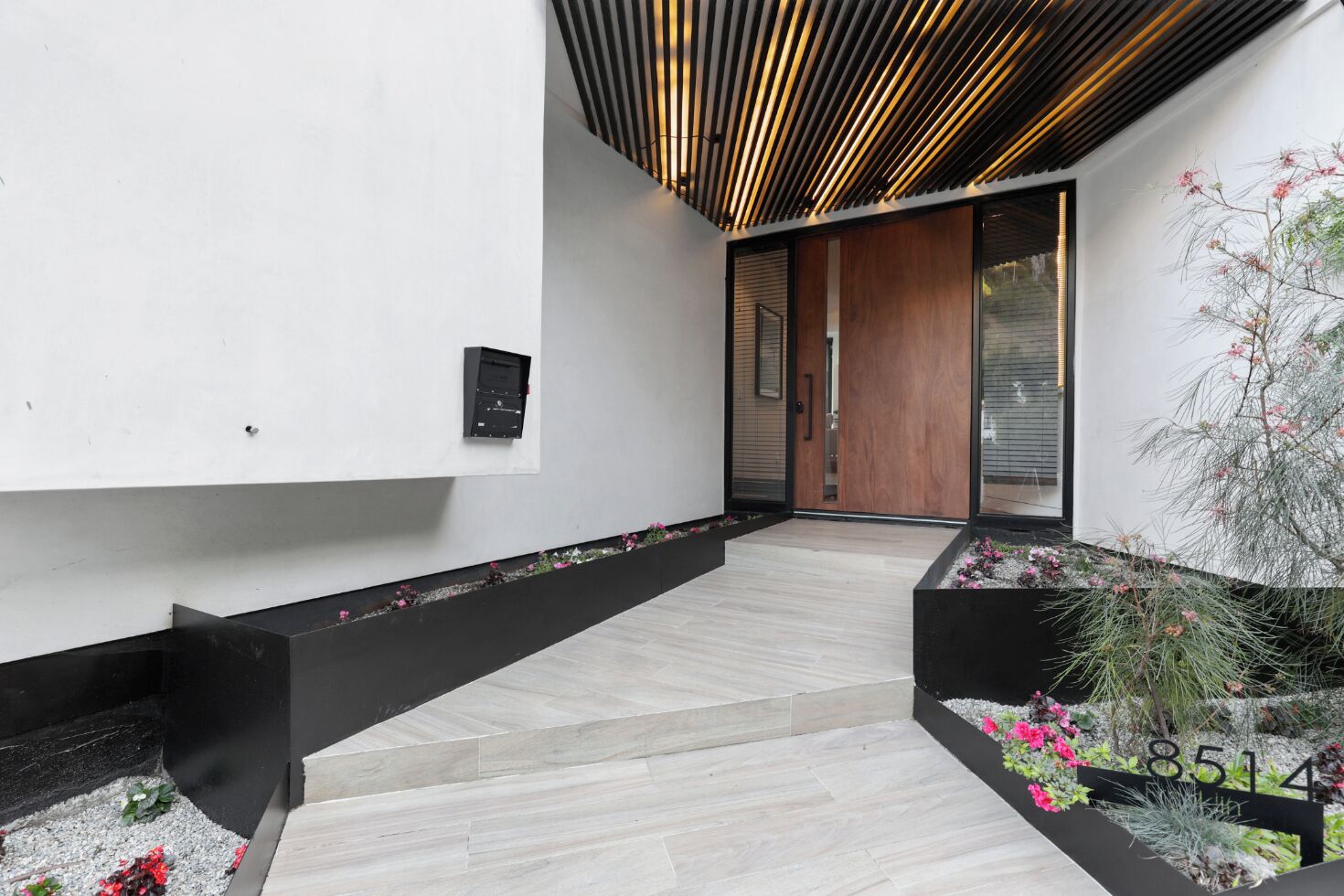 Een modern interieur met een houten plafond, een zwarte bank en een plantenbak met bloemen.