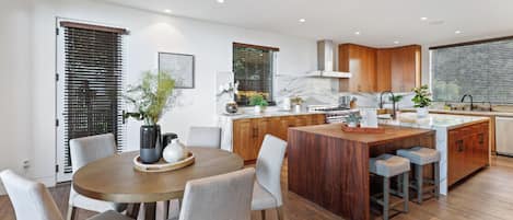 A modern kitchen with wooden cabinets, a central island, and a dining area with a round table and chairs.
