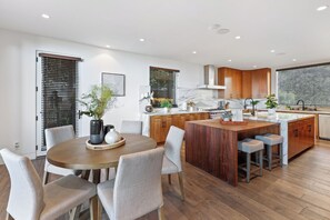 A modern kitchen with wooden cabinets, a central island, and a dining area with a round table and chairs. - Franklin Modern (West Hollywood)