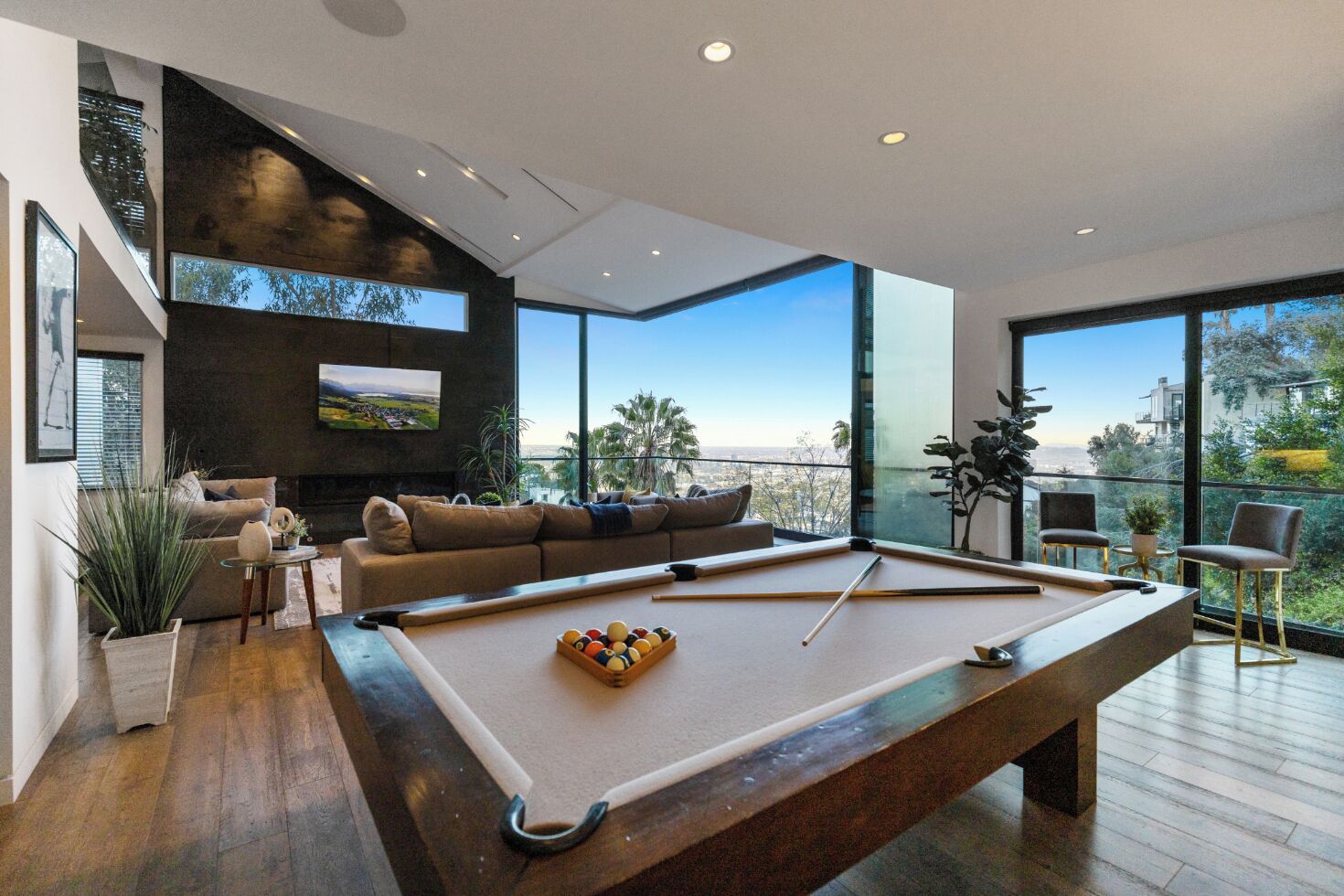 Una sala de estar moderna con mesa de billar, sofá y un amplio ventanal con vista a la ciudad.