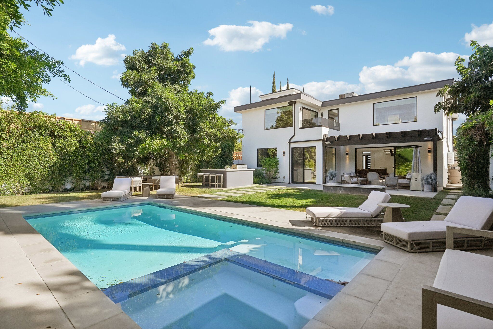 A modern two-story house with a swimming pool, outdoor seating, and a well-maintained garden.