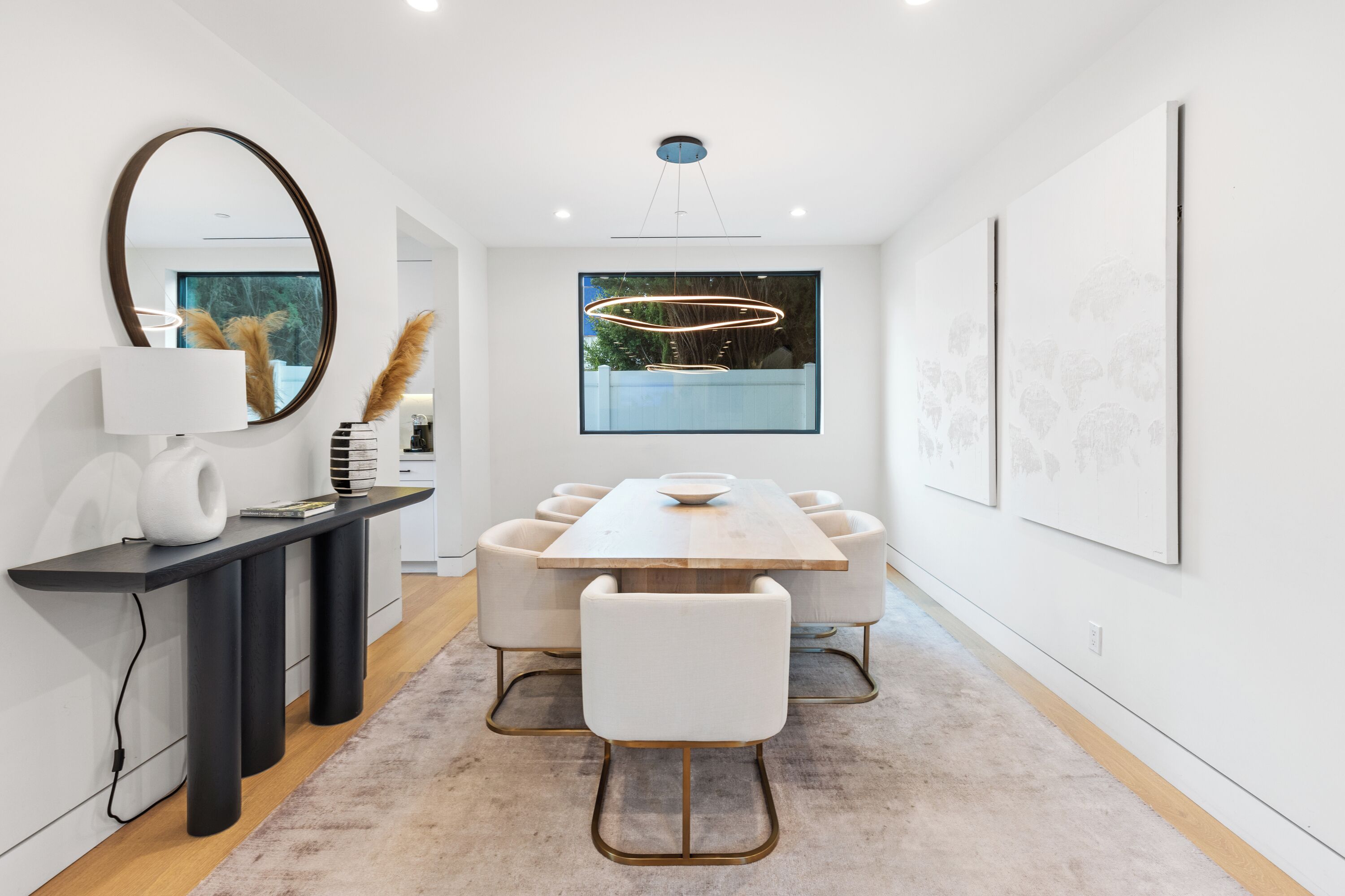 A modern dining area with a long table, white chairs, a black console, and a large mirror.