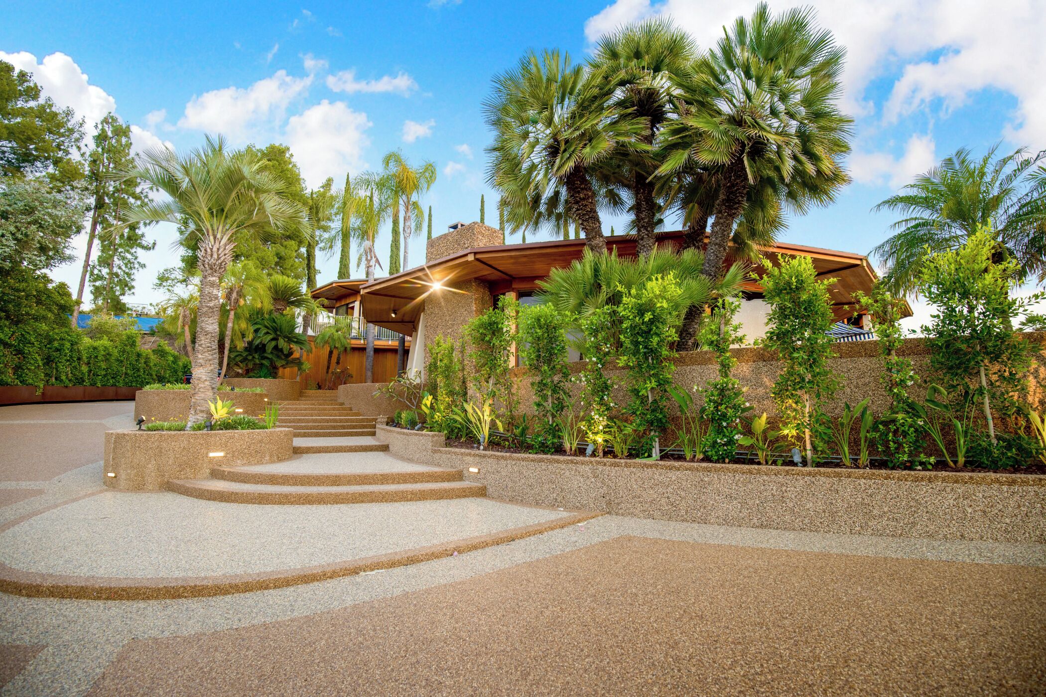 A modern building with a stone facade, palm trees, and a well-maintained garden.