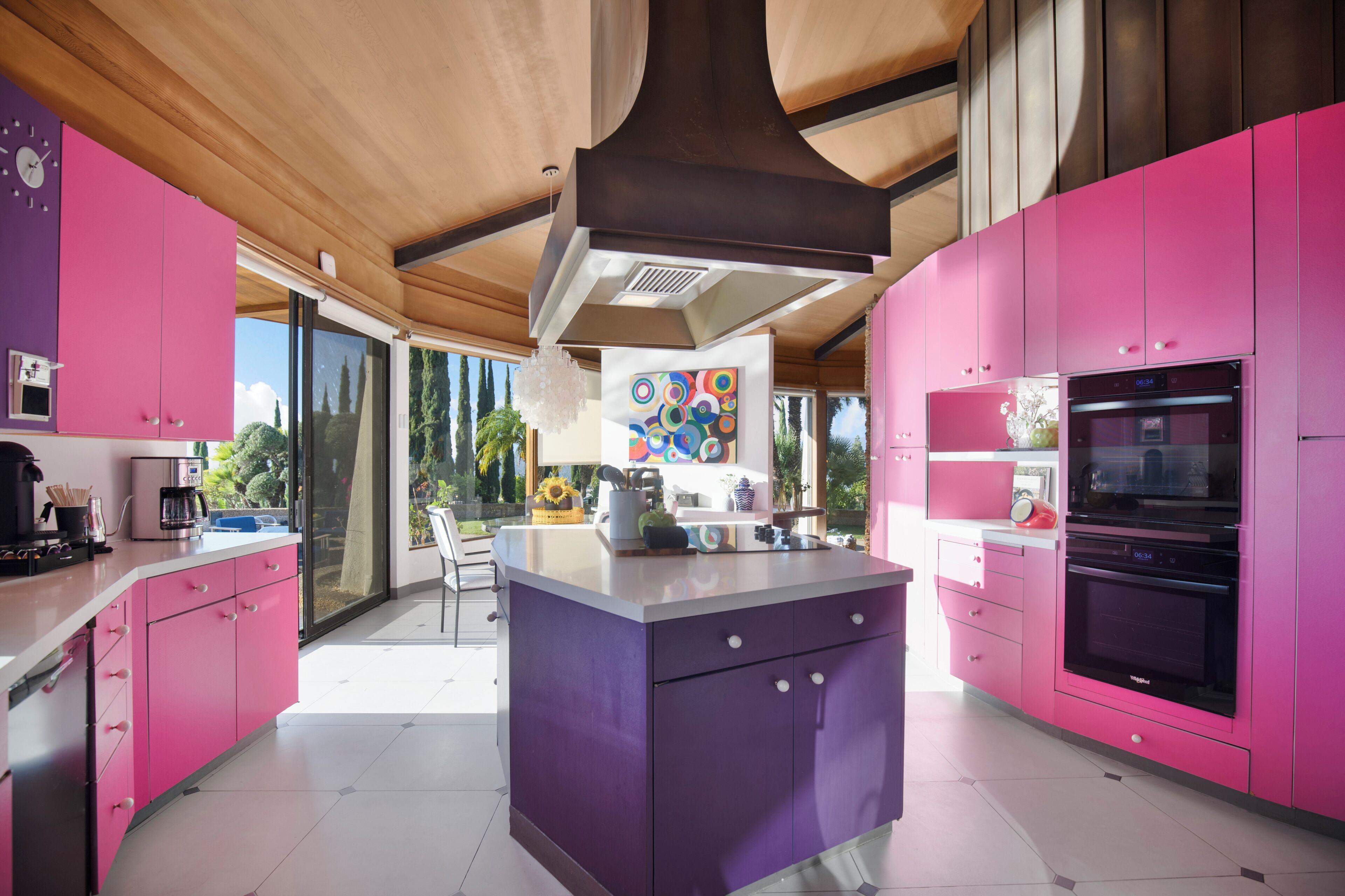 Una cucina moderna con mobili rosa, un'isola centrale e un'ampia finestra con vista sull'esterno.