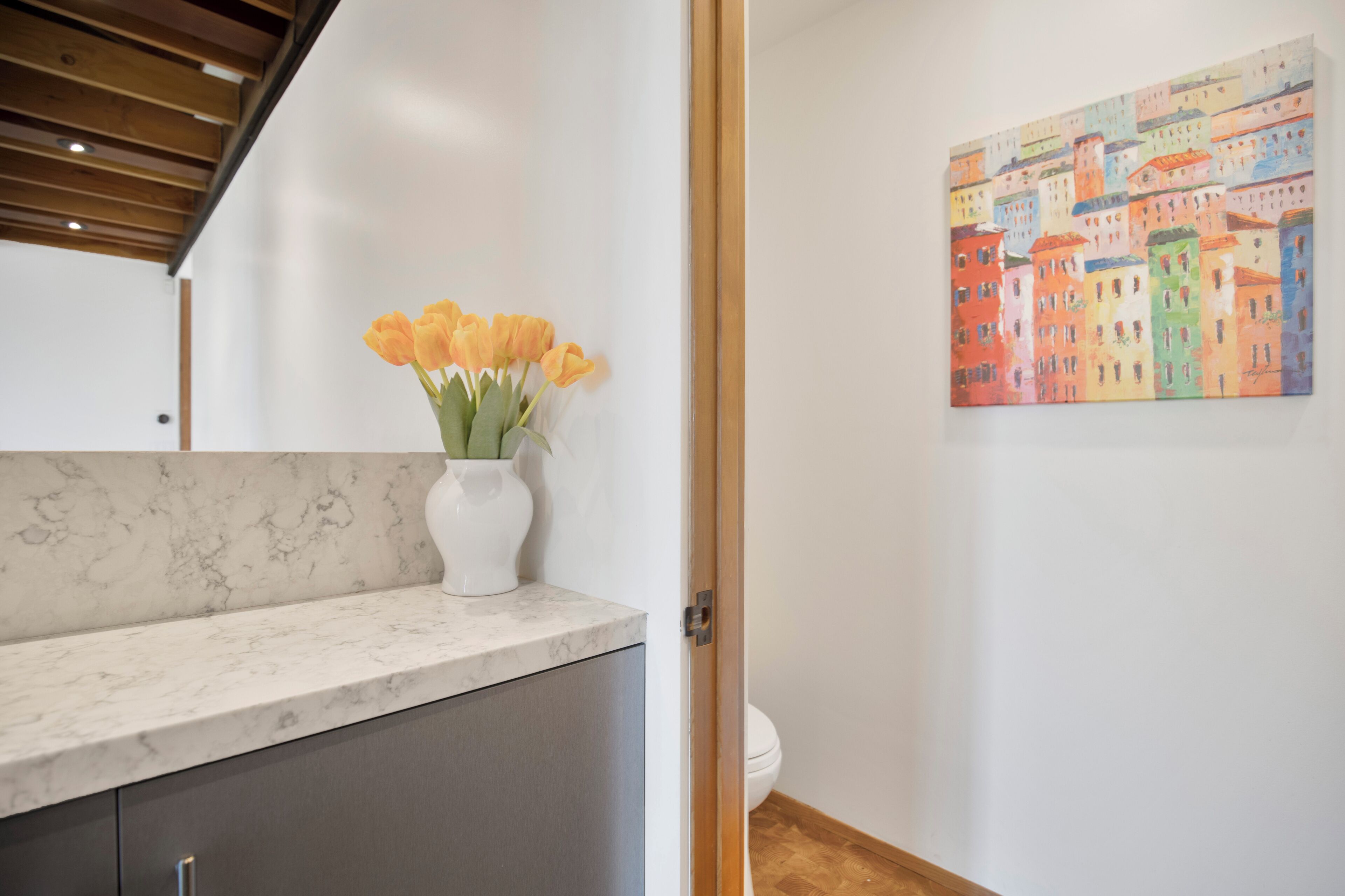 A bathroom with a marble countertop, a white vase with flowers, and a colorful painting on the wall.