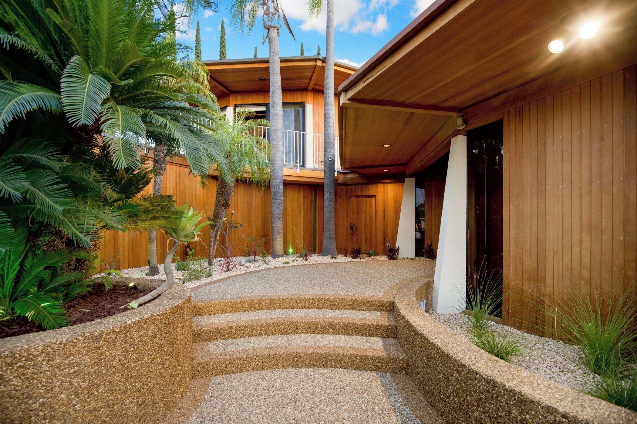 A modern building with a wooden facade, a curved driveway, and tropical plants.