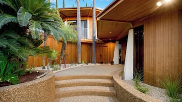A modern building with a wooden facade, a curved driveway, and tropical plants.