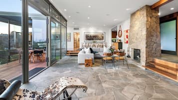Uma sala de estar moderna com lareira de pedra, porta de vidro para um deck e área de jantar com móveis de madeira.