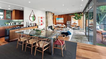 Cozinha moderna com mesa de jantar de vidro e cadeiras de madeira, lareira de pedra e uma grande janela com vista para um deck.