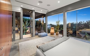 Quarto moderno com uma janela ampla, cama, área de estar e vista para o exterior.