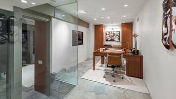 A modern office space with a glass partition, a desk with a chair, a wooden cabinet, and a wall-mounted artwork.