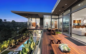 Ein modernes Haus mit einer Holzterrasse, Sitzgelegenheit im Freien und einem Pool.