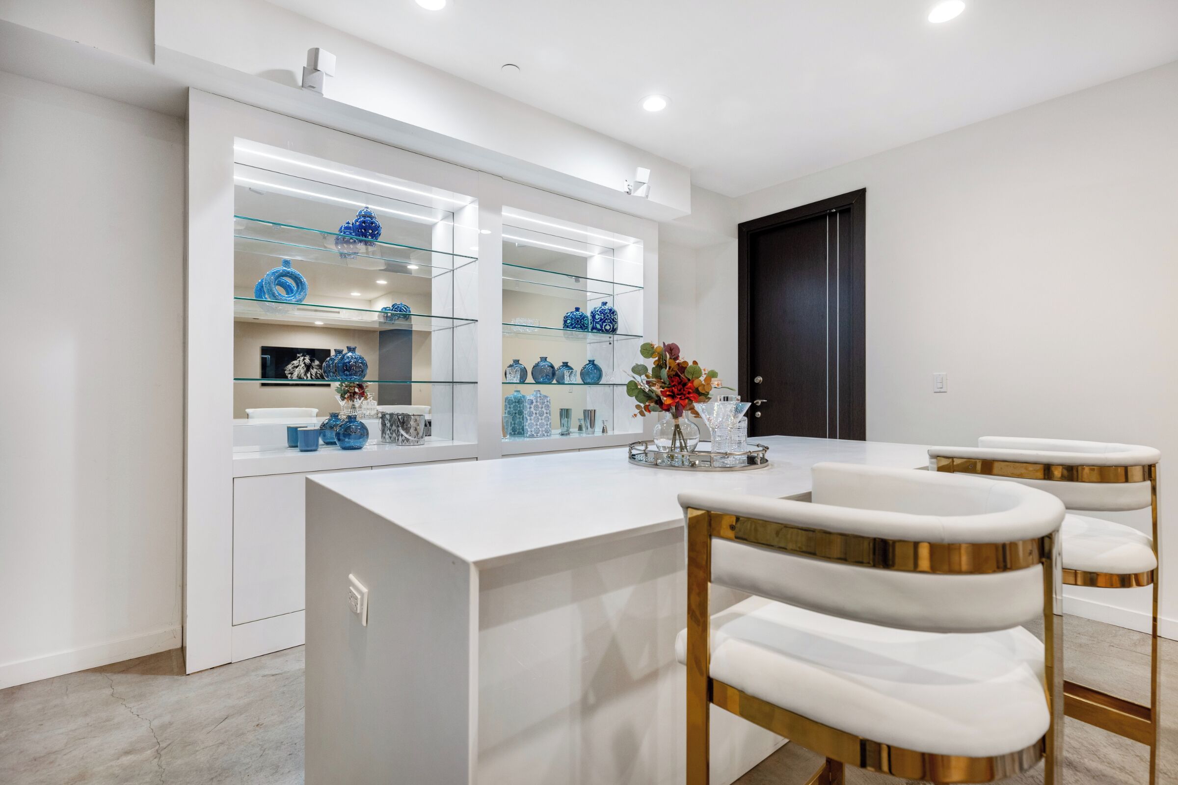 A modern kitchen with white cabinetry, a glass display shelf with blue decorative items, and a white countertop.