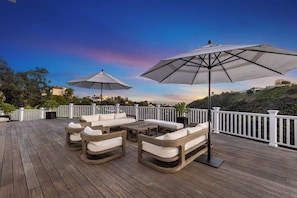 A wooden deck with outdoor furniture and umbrellas, overlooking a scenic landscape. - Stradella Hideaway (Los Angeles)