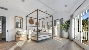 Une chambre spacieuse avec un lit à baldaquin, de grandes fenêtres et une vue sur la verdure environnante.