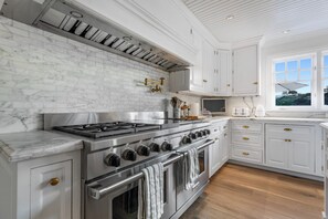 A modern kitchen with white cabinetry, a stainless steel stove, and a large window providing a view of the outdoors. - Stradella Hideaway (Los Angeles)