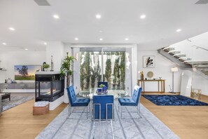 Una sala moderna con una mesa de comedor de vidrio, sillas azules, una chimenea y una escalera.