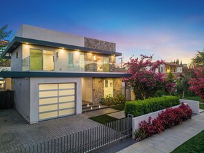 Uma casa moderna de dois andares, com garagem, um jardim bem cuidado e céu claro.