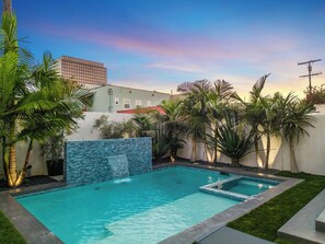 Piscina rectangular con una cascada, rodeada de palmeras y un muro de piedra.