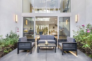 An outdoor seating area with two sofas and a table, surrounded by glass doors leading to an interior space. - Lindenhurst (Los Angeles)