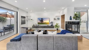 Un salon moderne avec un canapé gris, un téléviseur à écran plat, une cheminée et un balcon équipé d’un parasol.