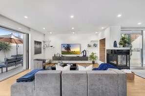 Uma sala de estar moderna com um sofá cinza, uma televisão de tela plana, uma lareira e uma varanda com guarda-sol.