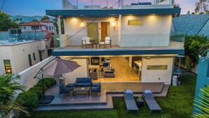 Une maison moderne à deux étages dotée d’un patio, d’un espace salon extérieur et d’une piscine.