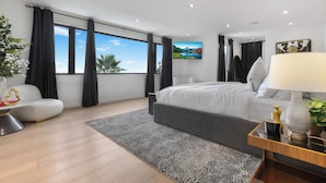 Quarto moderno com uma cama grande, uma escrivaninha com abajur, vista para o exterior e um quadro na parede.