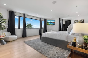 Ein modernes Schlafzimmer mit einem großen Bett, einem Schreibtisch, einem Stuhl und Blick ins Freie.