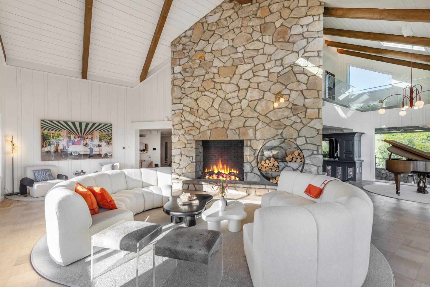 A spacious living room with a stone fireplace, white sofas, and a grand piano.