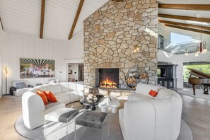 Ein großzügiges Wohnzimmer mit Kamin aus Stein, weißen Sofas und einem Flügel.