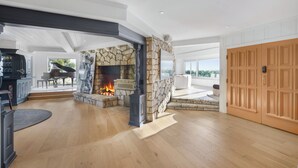Ein großzügiges Wohnzimmer mit Kamin aus Stein, einem Klavier und einer großen Holztür.