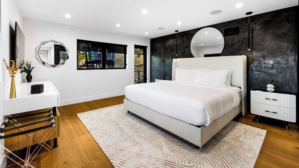 Un dormitorio moderno con una cama grande, una mesita de noche, un espejo y vistas al exterior.